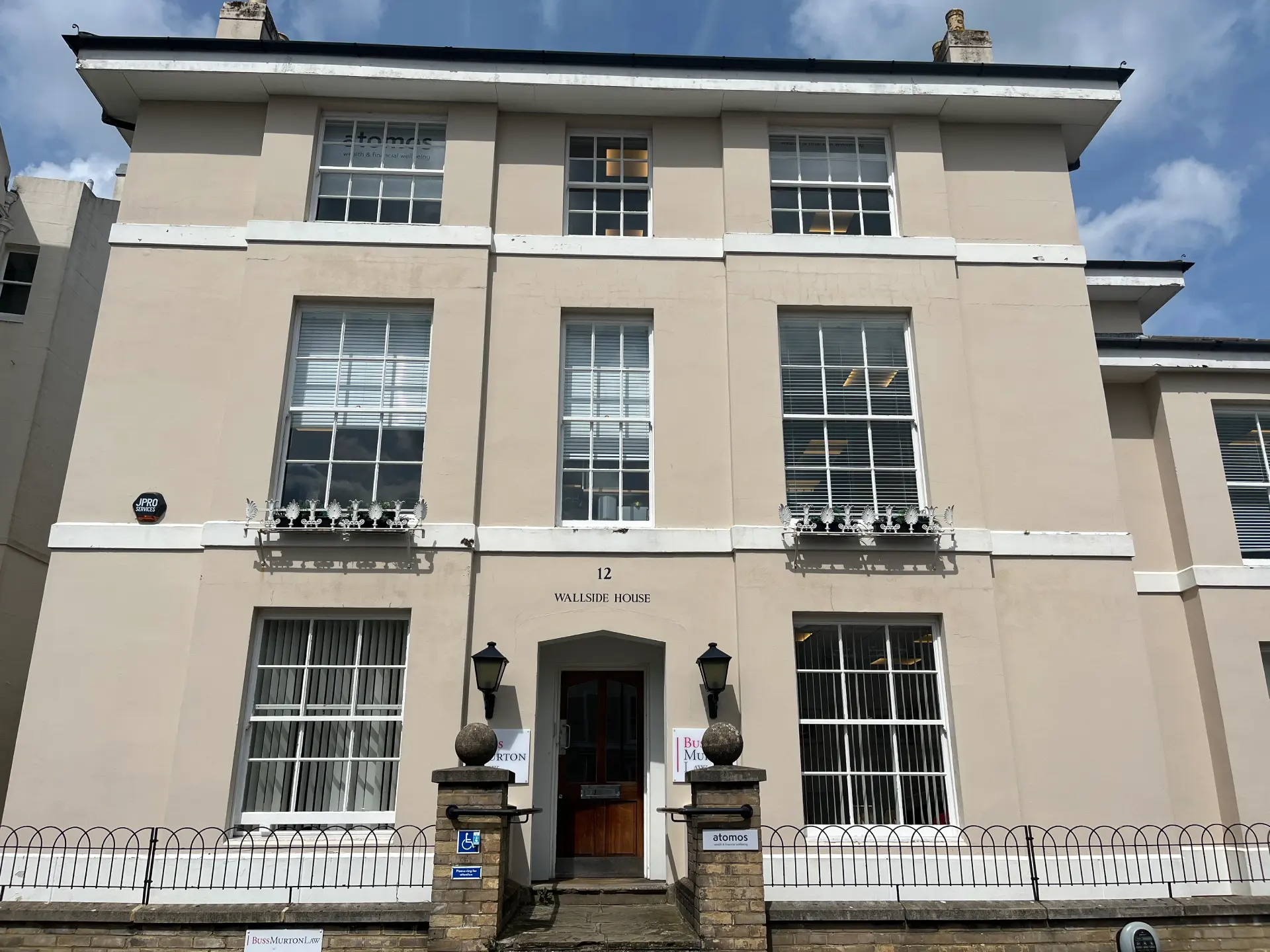 Wallside House at 12 Mount Ephraim Road, Tunbridge Wells: a three-storey Regency stuccoed townhouse in pale stone, with two wrought-iron juliet balconies on the first floor, a slate roof with two dormer windows, and two black iron lamp posts flanking the front door under the carved 12 Wallside House plate.